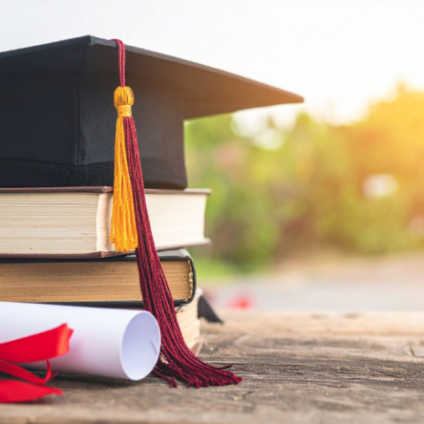 stack of books with graduation cap on top with sunshine behind
